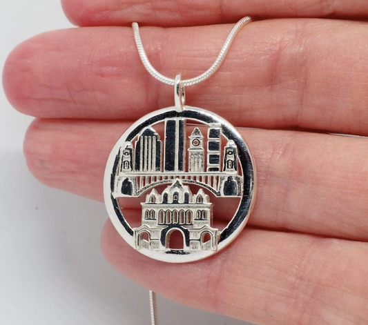 Silver necklace pendant with architectural design held between fingers on a white background